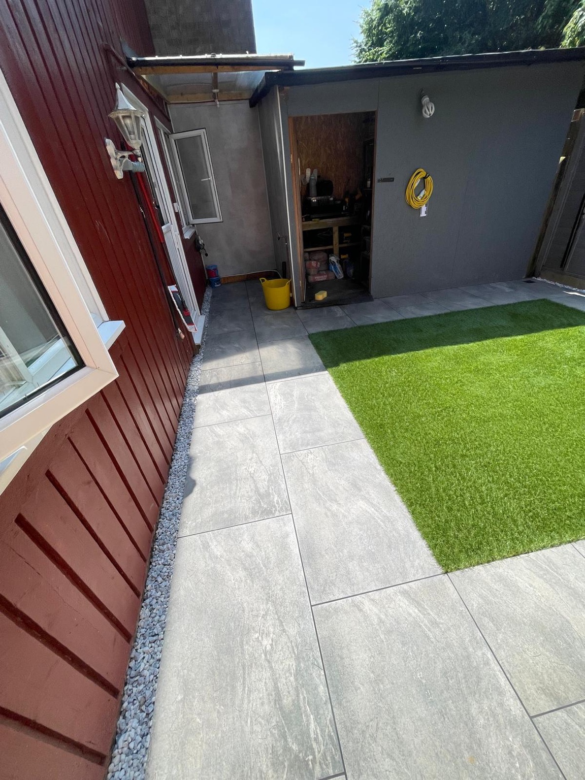 Paved walkway alongside the artificial grass and outbuilding
