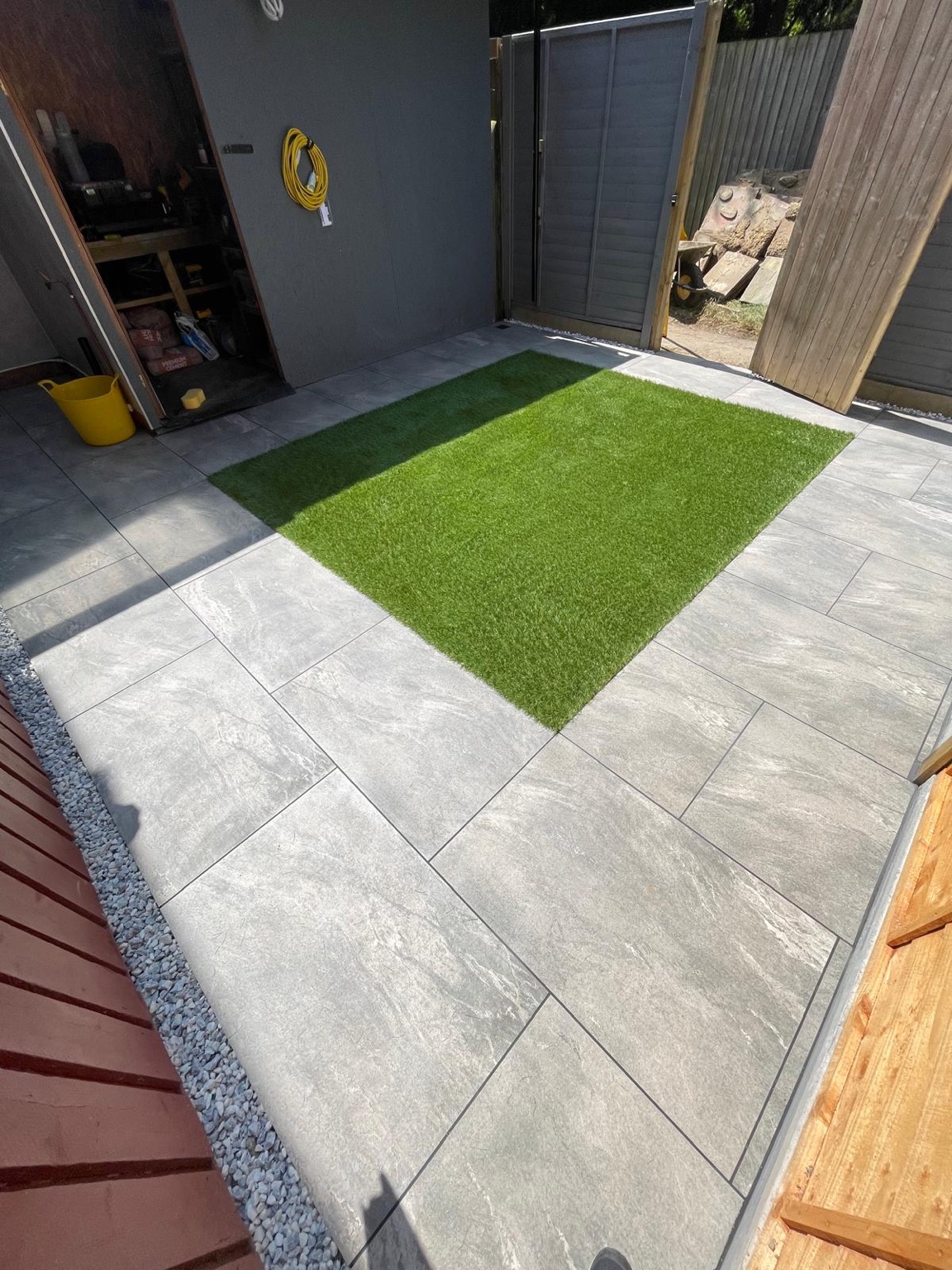 Large pale paving slabs around the rectangular area of artificial grass