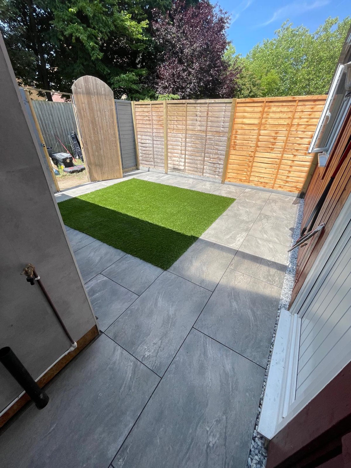 Wide view of a compact garden with artificial grass, pale paving and timber fencing