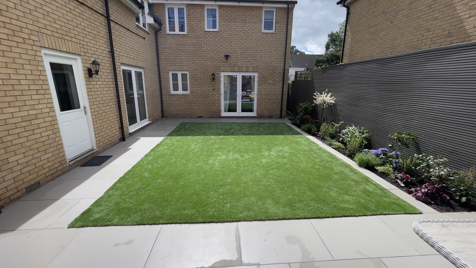 New lawn framed by planting beds, fencing and pale patio paving