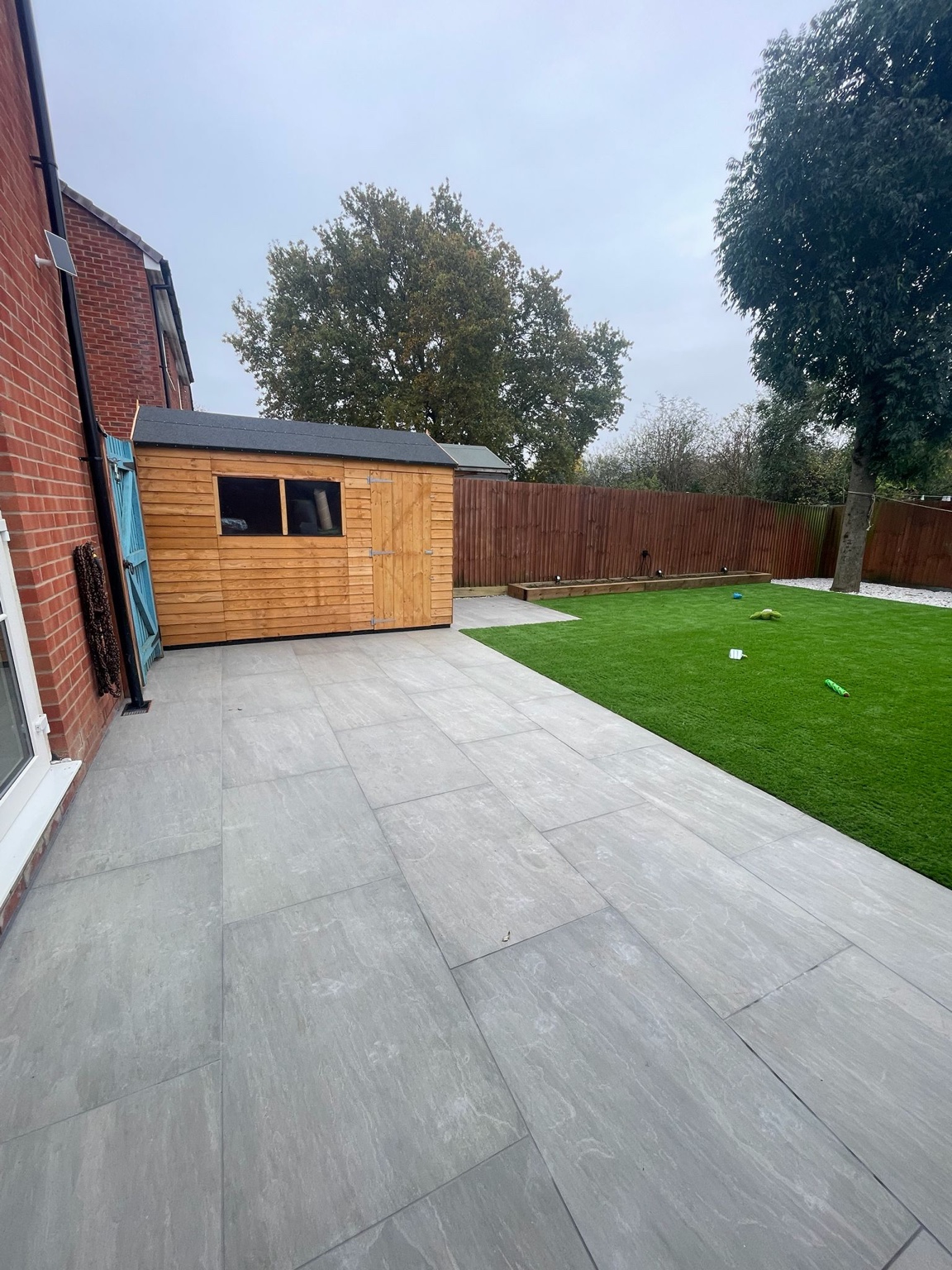 Paved patio beside the lawn and timber shed