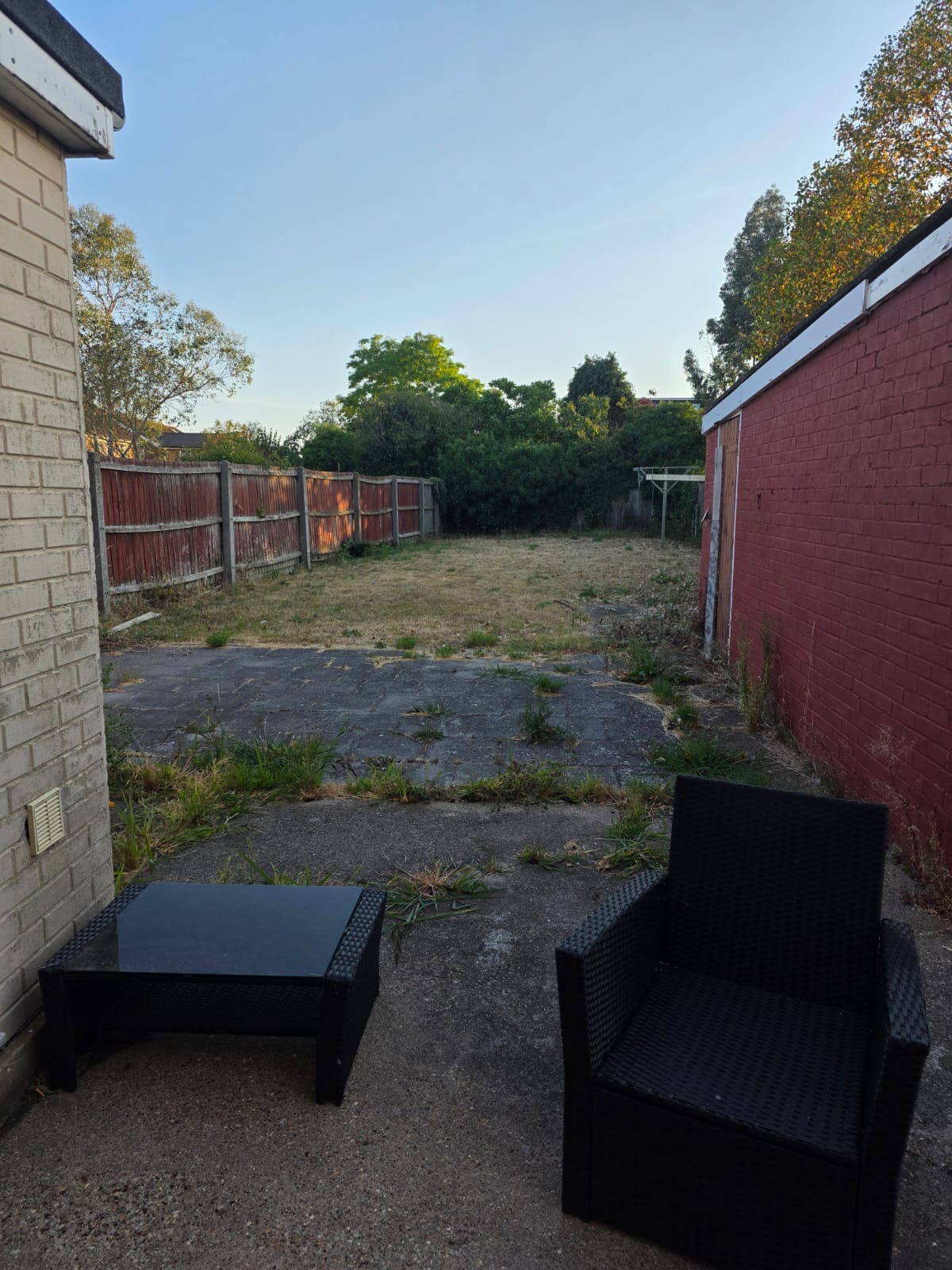 Garden before, with dry lawn and weeds between the patio slabs