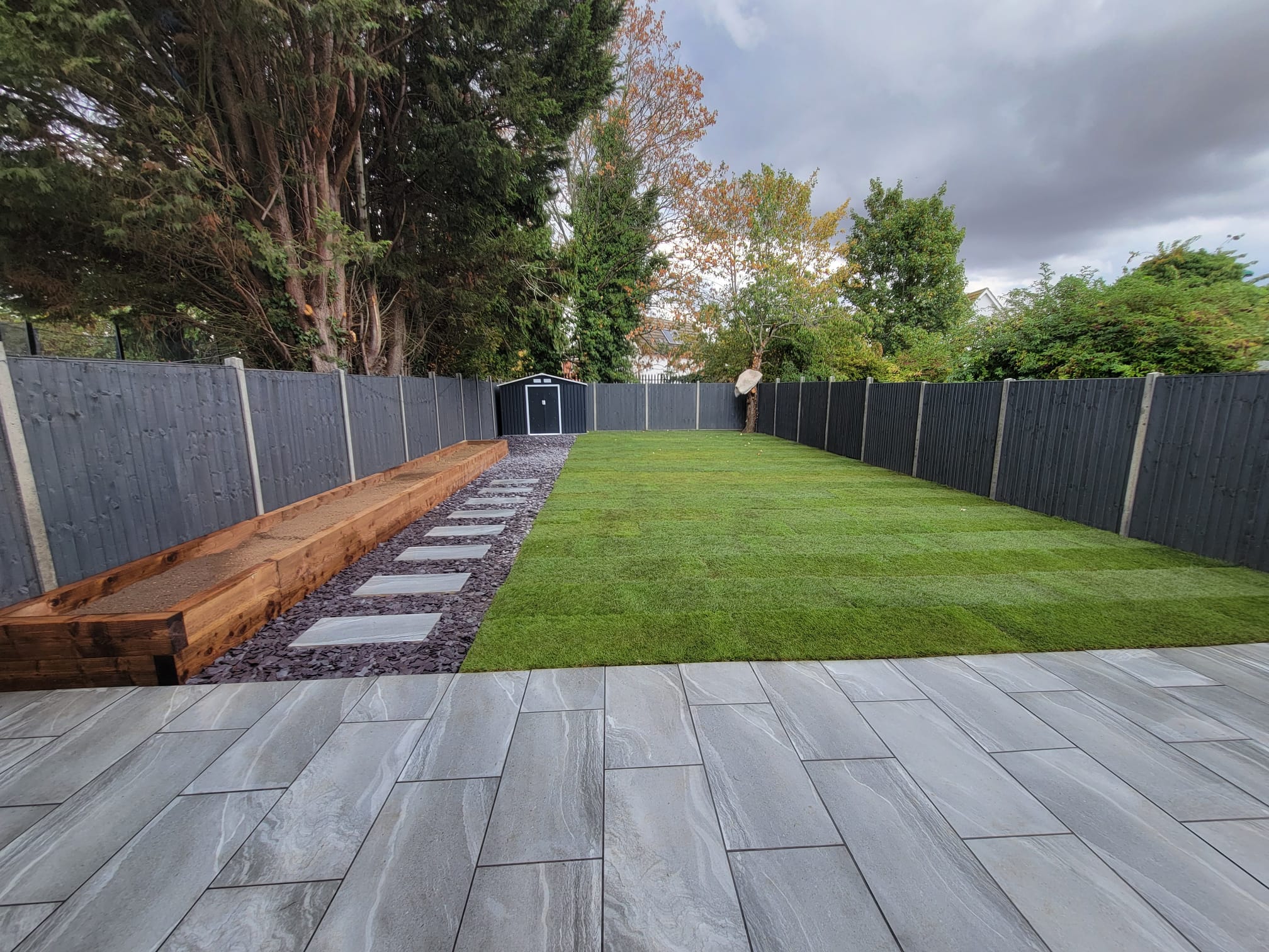 Wide view across a landscaped garden with lawn, sleepers and a patio