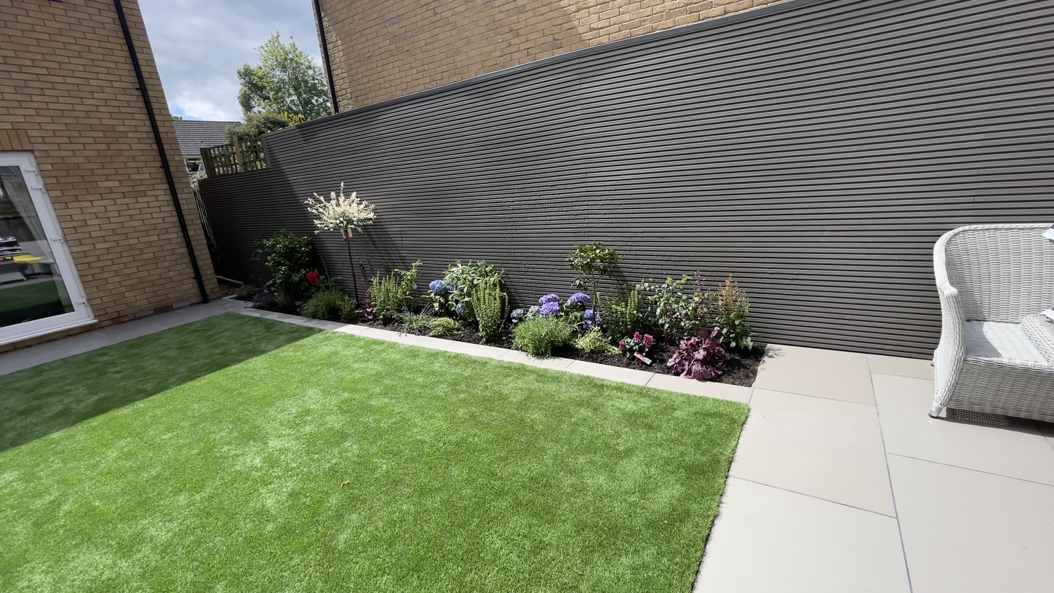 Fresh lawn with new plants beside a grey garden fence